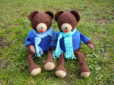 Zwei gehäkelte braune Teddybären mit blauen Pullovern und hellblauen Schals auf Gras