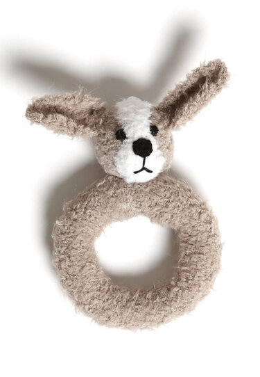 Gestrickte Babyrassel in Hasenform mit beigem Greifring, beige-weißes Fell und aufgestickte schwarze Augen und Nase, auf weißem Hintergrund.