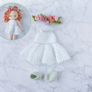 Weißes gehäkeltes Puppenkleid mit Blumenstirnband und hellgrünen Schuhen neben einer Amigurumi-Puppe.