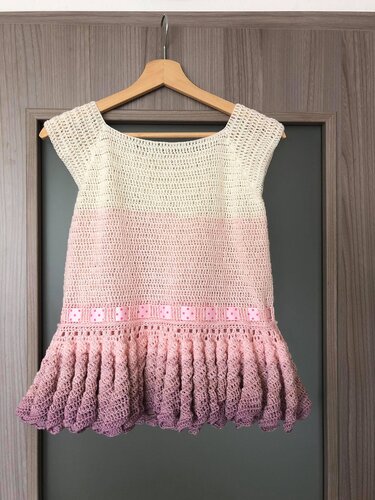 Ärmelloses gehäkeltes Puppenkleid in Creme, Rosa und Lila mit Rüschen und gepunktetem Schleifenband an einem Holzbügel