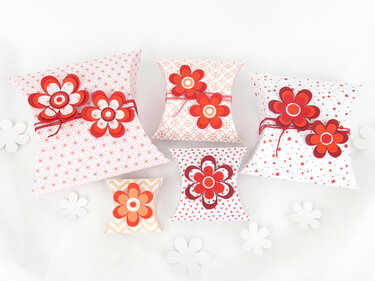 Mehrere gemusterte Papier-Kissenschachteln mit roten und orangefarbenen Papierblumen auf hellem Hintergrund