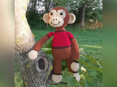 Brown and cream crocheted amigurumi monkey wearing a red shirt sitting on a tree branch