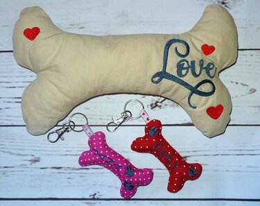Beiges gepolstertes Knochenkissen mit 'Love' Stickerei und zwei kleine rote und pinke Knochen-Schlüsselanhänger mit Karabinern