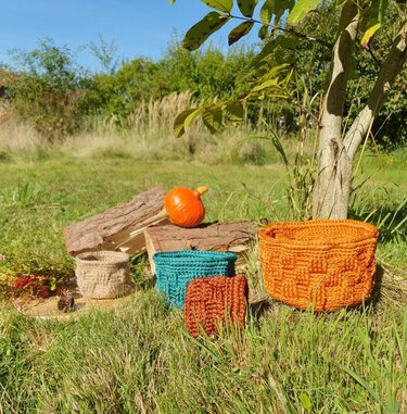 Handgehäkelte Körbe in Herbsttönen arrangiert auf Wiese mit Kürbis und Holzscheiten