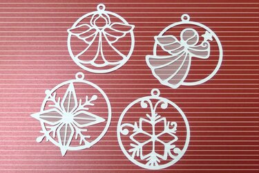 Vier weiße, filigrane Weihnachtsanhänger mit Engeln und Schneeflocken auf rotem Hintergrund