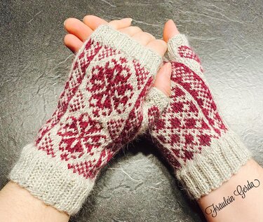 Detailansicht gestrickter fingerloser Armstulpen mit zweifarbigem Fair-Isle-Muster, Rippbündchen und Daumenöffnung