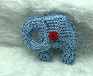 Hellblauer gehäkelter Elefant mit roter Blüte auf weißem Hintergrund