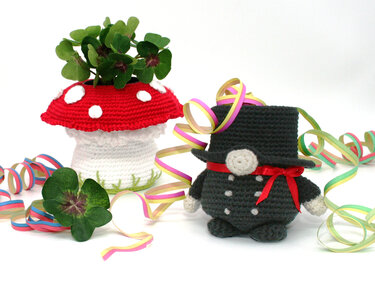 Crocheted mushroom pot with clovers beside an amigurumi chimney-sweep figure and colorful streamers.