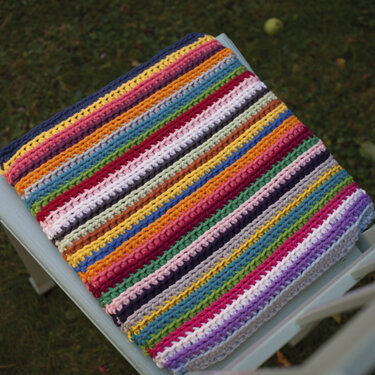 Gehäkeltes Quadrat mit bunten Streifen, gefaltet auf einem Stuhl