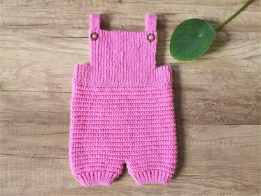 Rosa gehäkelter Babystrampler mit Holzknöpfen auf Holzuntergrund