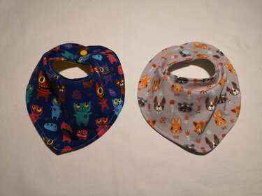 Zwei Bandana-Halstücher nebeneinander: links blaues mit Monster-Motiv, rechts hellgraues mit Tiermotiven, beide mit Druckknopf