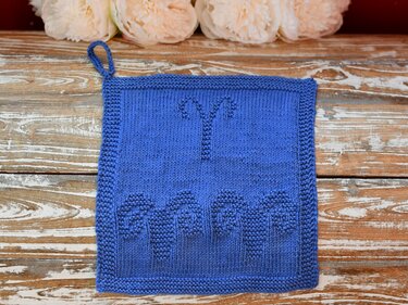 Blauer gestrickter Topflappen mit Widder-Symbol, Reliefmuster und Aufhängeschlaufe auf Holzuntergrund