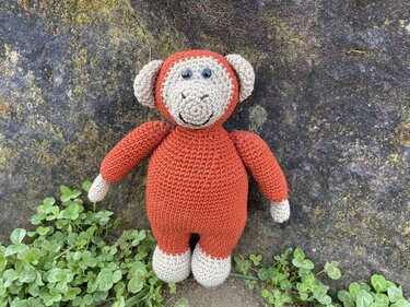 Rostrot-beiger gehäkelter Amigurumi-Affe mit Knopfaugen vor steinigem Hintergrund
