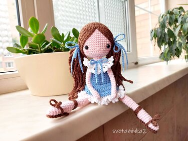 crocheted amigurumi doll with brown yarn hair and blue dress sitting on a windowsill