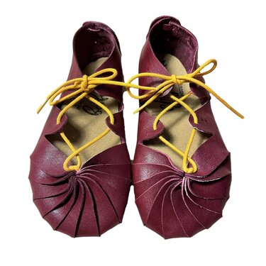 Zwei burgunderrote Lederschuhe mit gelben Schnürsenkeln und spiralförmigem Faltenwurf an der Spitze.