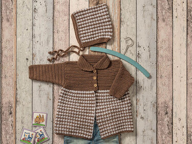 Gehäkelte Babyjacke mit Knöpfen und passende Mütze in Braun und Weiß mit Karomuster auf Holzbrett-Hintergrund