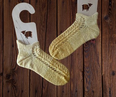 Goldgelbe gestrickte Damensocken mit Zopf- und Lochmuster auf Holzsockenspannern mit Schaf-Motiv vor dunklem Holz