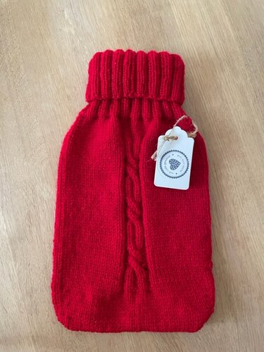 Roter gestrickter Wärmflaschenbezug mit Zopfmuster und Umschlagkragen auf Holz
