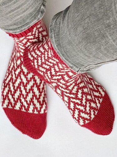 Gestrickte Damensocken in Rot und Weiß mit Zickzackmuster an Füßen mit grauer Hose