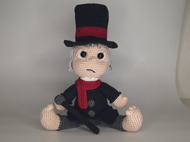 Gehäkelte Amigurumi-Puppe sitzend mit schwarzem Zylinderhut, rotem Schal und Gehstock