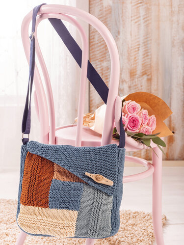 Gestrickte Umhängetasche mit Patchwork-Muster und Holzknopf an einem rosa Stuhl