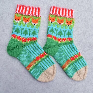 Paar bunter gestrickter Socken mit Fuchsgesichtern, Bäumen und Pilzen