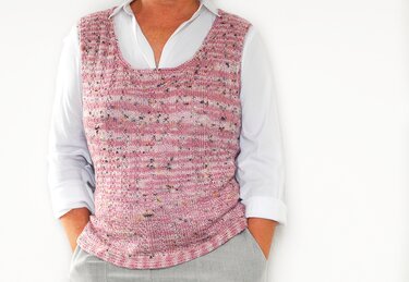 Frau trägt rosafarbenen gestrickten Pullunder mit Sprenkeln über weißer Bluse, Hände in Hosentaschen