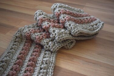 Gehäkelter Schal in Beige und Rosa mit Reliefstreifen auf Holzboden