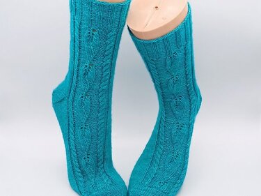 Türkise gestrickte Socken mit Zopf- und Blatt-Ajourmuster auf Modellfüßen