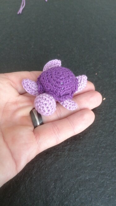 Kleine, schnell gehäkelte Schildkröte in Lila auf geöffneter Hand