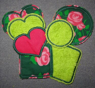 Gestickte Pads in Herz-, Kreis- und Quadratform aus grünem Frottee und rosengemustertem Stoff.