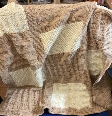 Gestrickte Babydecke in beige und creme mit quadratischen Feldern und Zopf- sowie Krausrippenmustern