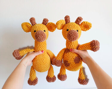 Hands holding two yellow and brown crocheted amigurumi giraffe toys, one spotted