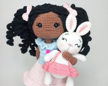 Crocheted amigurumi girl with black curly hair holding a white bunny in a pink dress