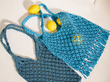 Detailaufnahme zweier Makramee Netzbeutel mit offenem Knotenmuster, geflochtenen Henkeln und Fransen; eine Tasche enthält Zitronen