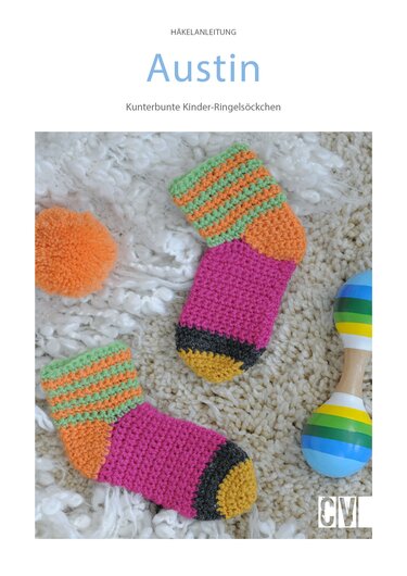 Zwei bunte gehäkelte Kinder-Ringelsöckchen in Pink, Orange, Grün und Gelb auf cremefarbenem Flausch, daneben eine Rassel und ein Bommel.