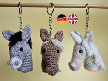 Drei gehäkelte Amigurumi-Pferdeköpfe in Grau, Braun und Pastell an Metall-Schlüsselringen