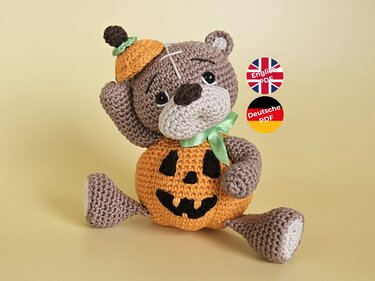 Sitzender gehäkelter Teddybär mit orangefarbenem Kürbis‑Körper und kleinem Kürbishut
