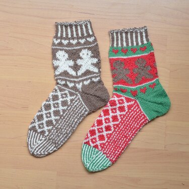 Zwei gestrickte Weihnachtssocken in Braun-Weiß und Rot-Grün mit Lebkuchenmann- und Rautenmuster