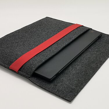 Dunkelgraue Filztasche mit rotem Gummiband, in der ein schwarzes Notebook steckt.