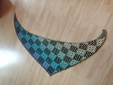 Gestricktes Dreieckstuch mit schwarz und türkis gemustertem Rautenmotiv auf Holzfußboden