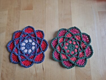 Zwei gehäkelte Blumenuntersetzer in Blau-Rot und Grün-Pink auf Holztisch