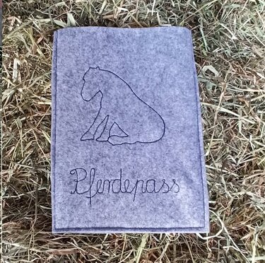 Graue Filzhülle mit gesticktem Pferdeumriss und Schriftzug „Pferdepass“ auf Heu