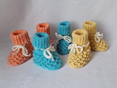 Nahaufnahme gestrickter Babyschuhe mit Rippbündchen, Lochmuster und weißer Kordel