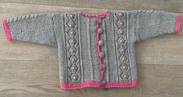 Gestrickte hellgraue Kinderjacke mit rosa Kanten, mittiger Knopfleiste und aufgenähten rosa Blüten an beiden Vorderseiten