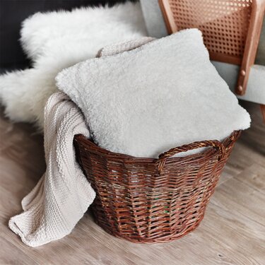 Geflochtener Korb mit gestrickter Decke und flauschigem Kissen