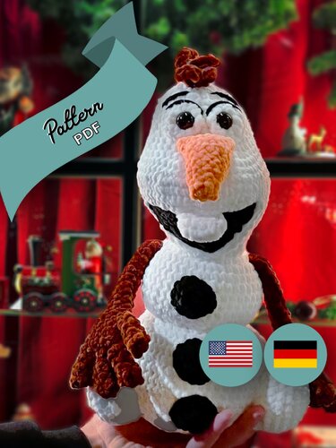 White crocheted snowman amigurumi with carrot nose, black button spots and brown arms held in front of a holiday display; PDF and language badges visible.