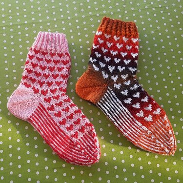 Zwei gestrickte Socken mit weißem Herzmuster auf grünem gepunktetem Stoff
