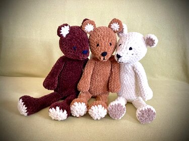 Drei handgehäkelte Amigurumi-Teddys in bordeaux, hellbraun und weiß nebeneinander