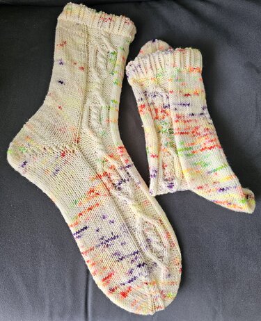 Nahaufnahme zweier gestrickter Socken in Creme mit bunten Sprenkeln und sichtbarem Zopfmuster